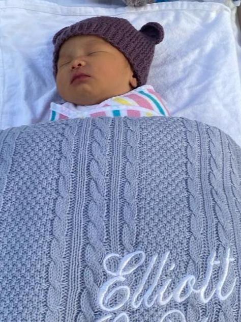 Baby in a cot with a grey personalised baby blanket to keep baby warm. Baby name is embroidered in white.