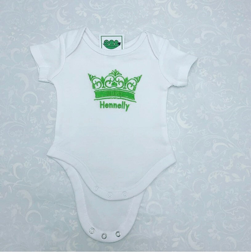 Personalised baby bodysuit with embroidered crown. The crown has the letters HRH on the band of the crown. Baby's name is embroidered underneath the crown. Embroidery in Green thread.