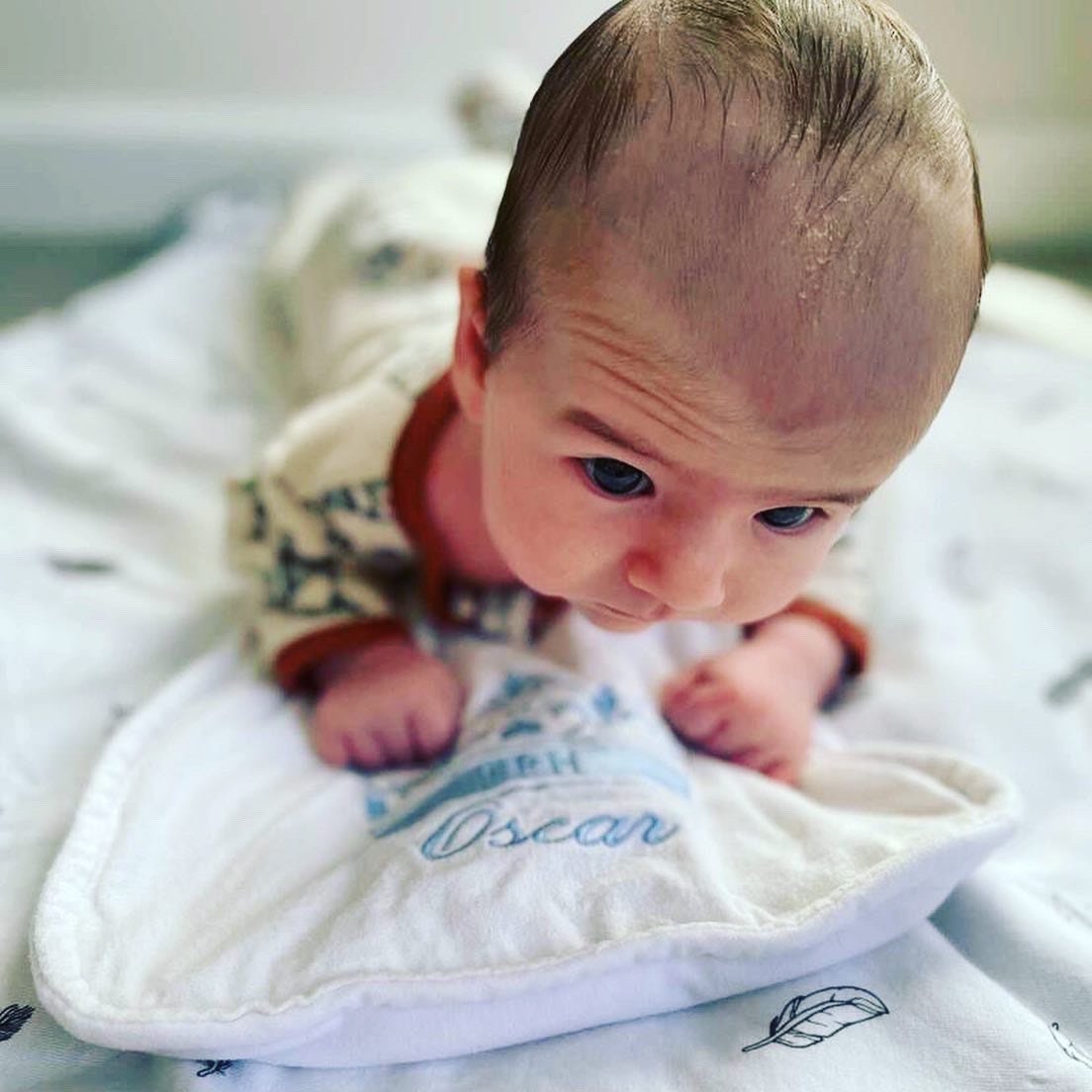 Personalised burp cloth with baby's name and a crown embroidered in blue thread is large enough for baby to use as a tummy time mat. Picture of baby using burp cloth as a tummy time mat. 