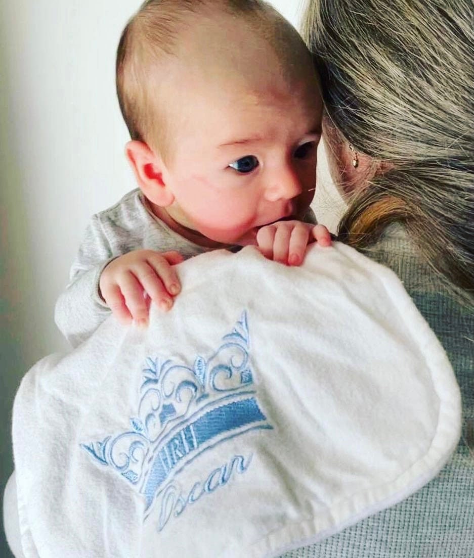 Burp Cloth with baby over Mother's Shoulders. Burp cloth has baby's name and a crown embroidered using blue thread colour..