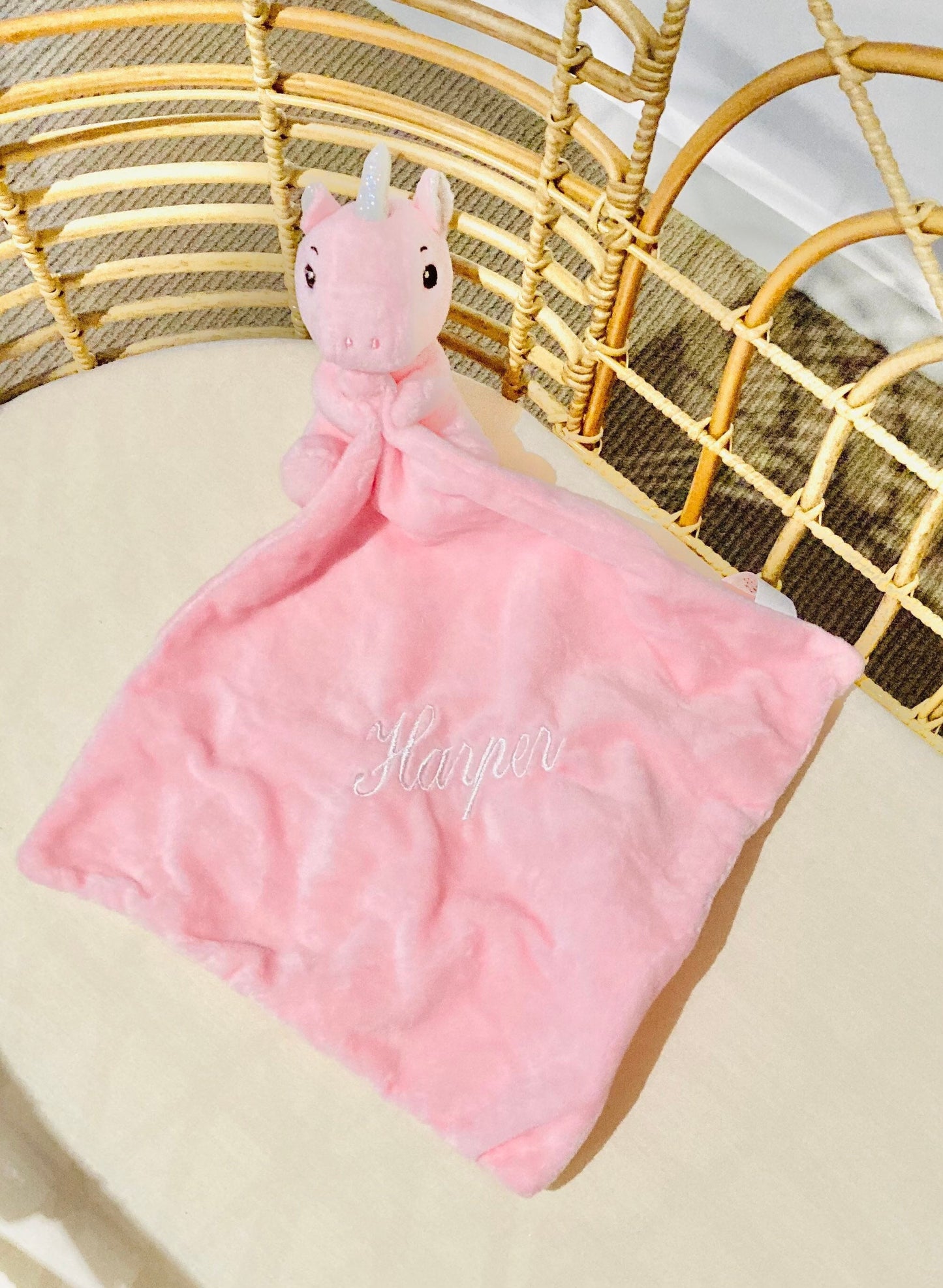 Unicorn baby comforter with a unicorn plush toy attached to a mini blankie embroidered with baby's name in white thread. 