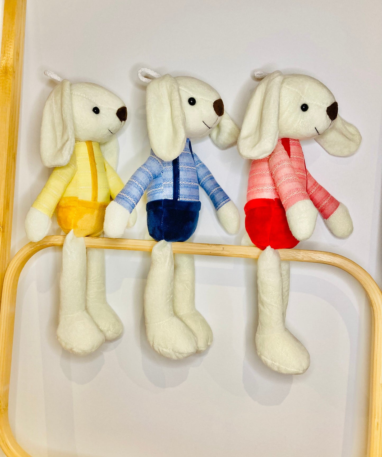 Plush bunnies in blue, yellow, and red overals. Personalised bunny on one ear with baby's name.