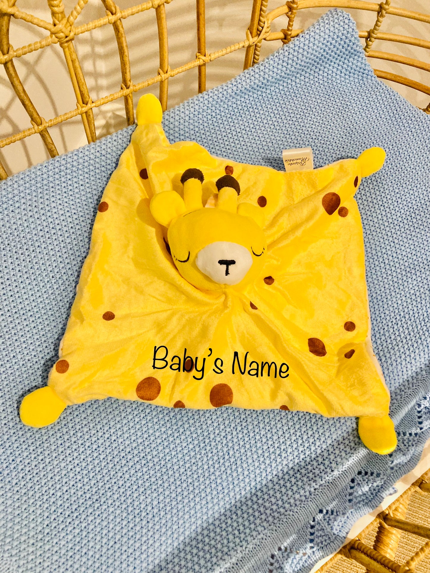 Yellow Giraffe with brown pokadots in a cot on top of a blue baby blanket. 