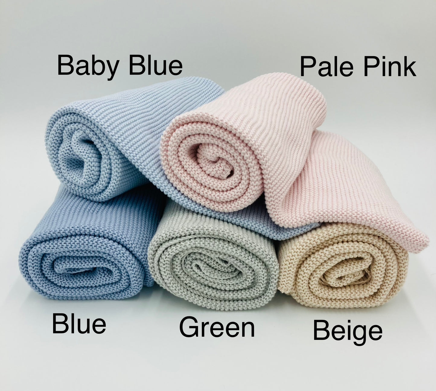 Raw edge cotton knit baby blankets rolled in a stack. Colours include Baby Blue, Pale Pink, Blue, Green and Beige.